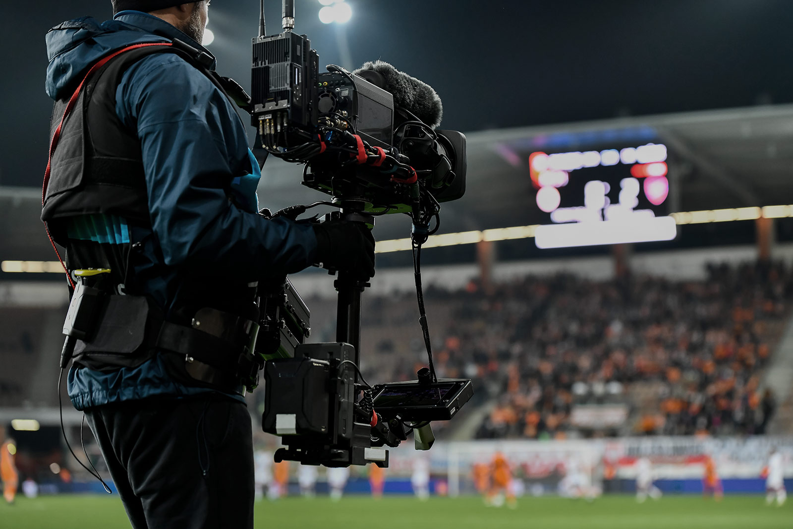 Broadcast camera operator filming a floodlit football occasion